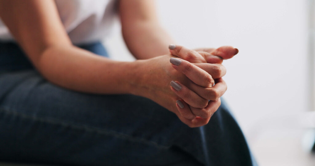 A person crosses their fingers with their hands rested on their knees.